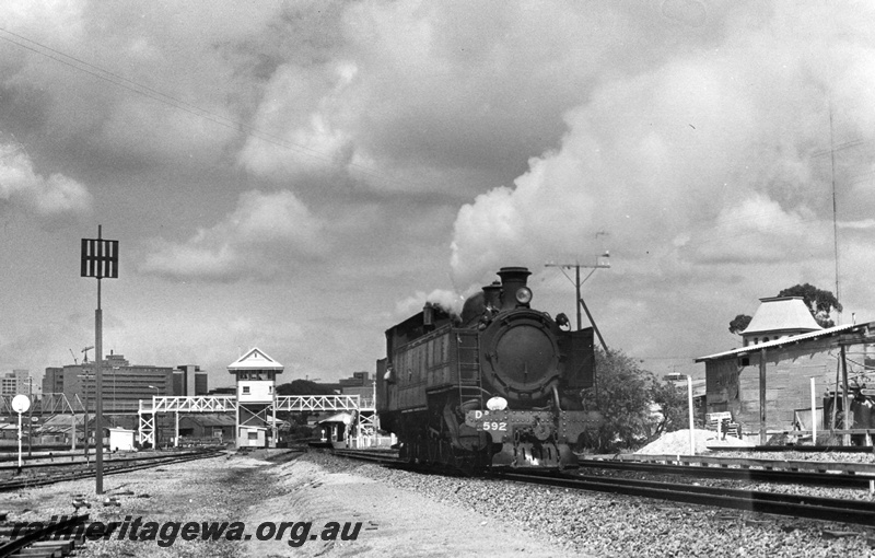 P02270
DD class 592, signal box, footbridge, East Perth, light engine, side and front view, white tail disc on the front buffer beam indicating that the loco is running bunker first, Royal Perth Hospital in the background
