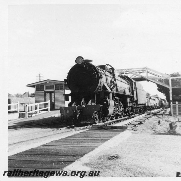 P03415
V class 1216 steam locomotive on goods train, front and side view, foot bridge, end of station building, Chidlow, ER line.
