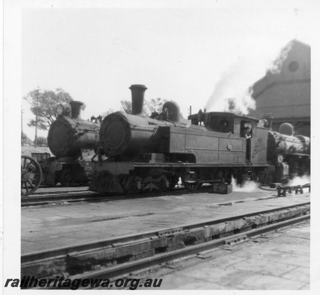 P03434
N class 201 steam locomotive, in steam at loco shed, front and side view, ash pit in foreground, East Perth, ER line.
