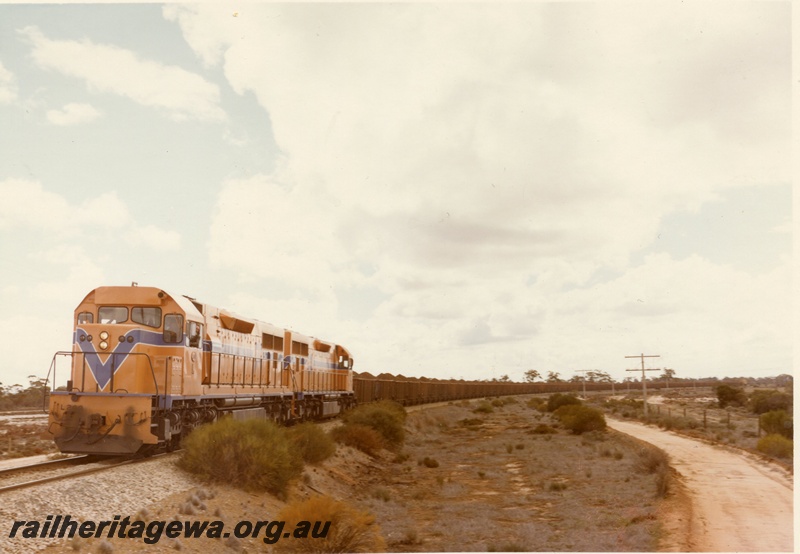 P03928
L class 269 standard gauge diesel locomotive, front and side view, in Westrail orange livery double heading another diesel locomotive in Westrail orange livery, on iron ore train, WO class iron ore wagons, on route to Kwinana, standard gauge line. 
