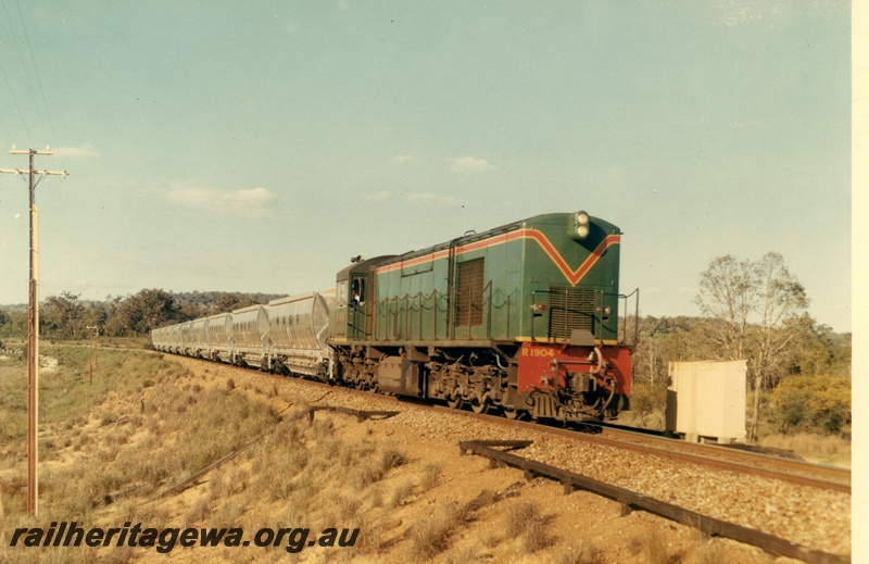 P03934
1 of 2, R class 1904 diesel locomotive in the green with red and yellow stripe livery, hauling a bauxite train of XC class wagons, side and front view

