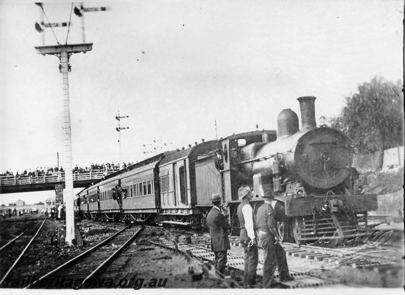 P04381
Commonwealth Railways (CR) G class steam locomotive, VB class van, ABP class carriages, side view of tender and loco, on the first passenger train from South Australia, passing under the Maritana Street bridge crowded with onlookers, arriving at Kalgoorlie. Kalgoorlie.
