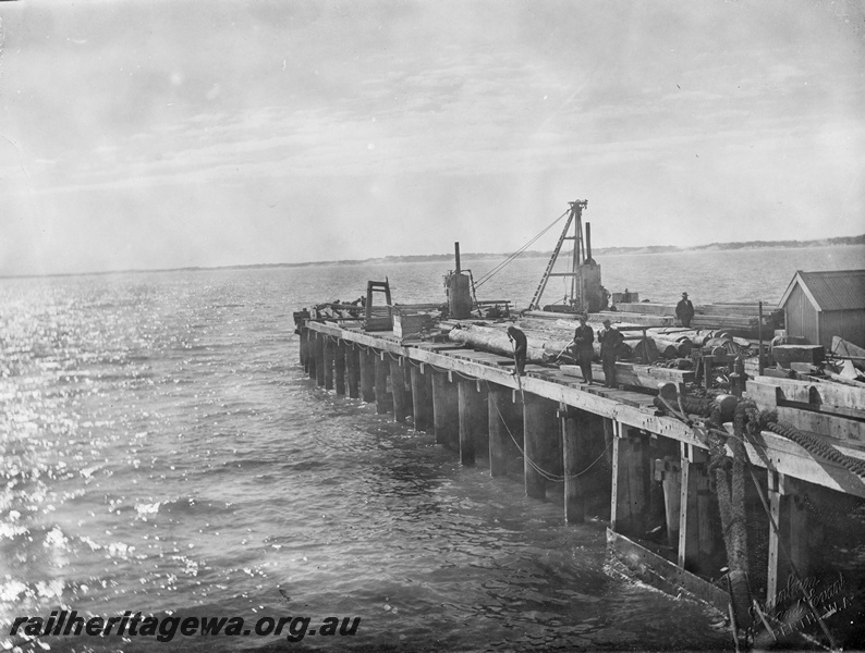 P10428
2 of 3 photos of construction of the Bunbury Jetty. There is no evidence of 'hi-vis' vests, safety hats or safety railing on edge of work site. Building to right possibly construction office and crane in right background.

