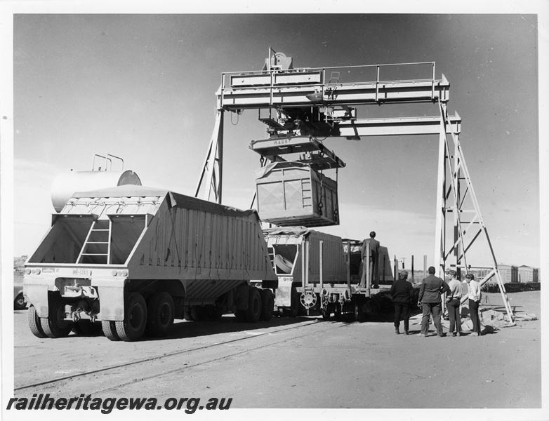 P10637
Bulk ammonium nitrate container, being emptied into road trailer by WAGR overhead gantry crane, group of onlookers, side view, Meekatharra
