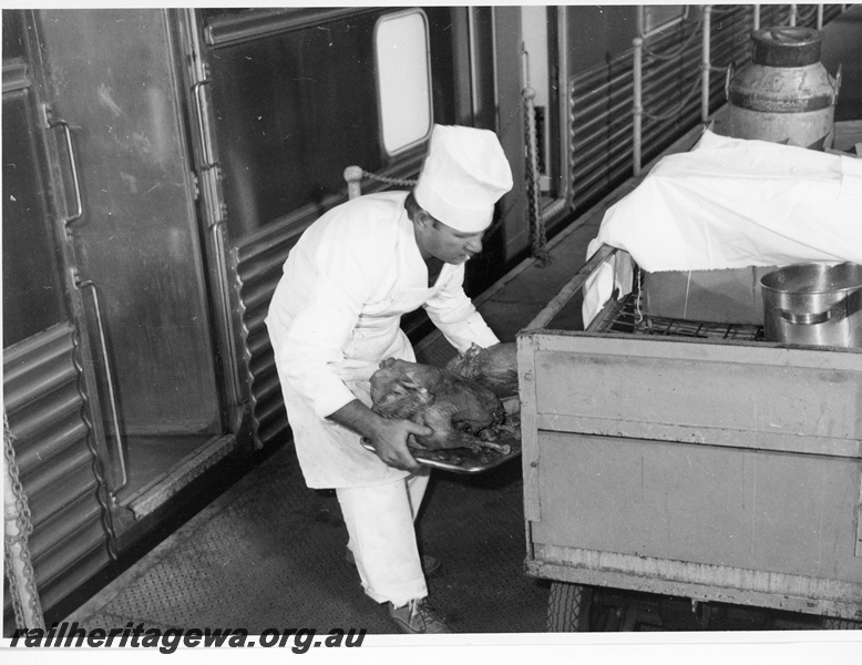 P10645
Train chef, loading tray of chicken, from food trolley on platform, into stainless steel carriage, close up view
