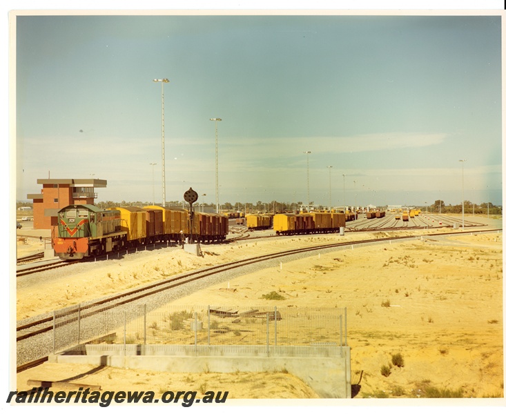 P10646
M class 1851, in green livery with red and yellow stripe, shunting wagons over the hump, control tower, shunters building (largely obscured), signal, assorted wagons in ladder sidings, culvert, Forrestfield marshalling yard, c1970
