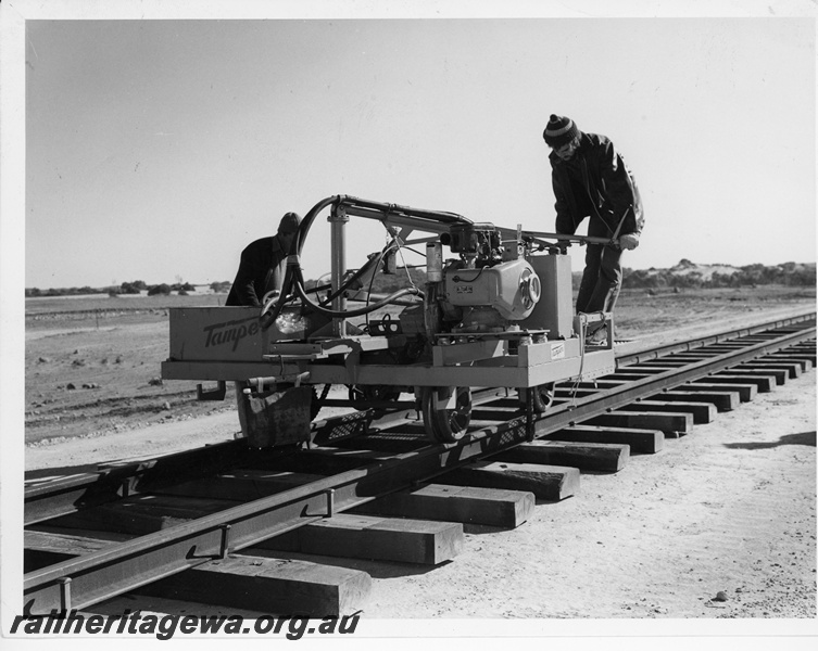 P10674
Tamper dog spike machine, driving in spikes on newly laid track, workers, Eneabba, DE line, end and side view 
