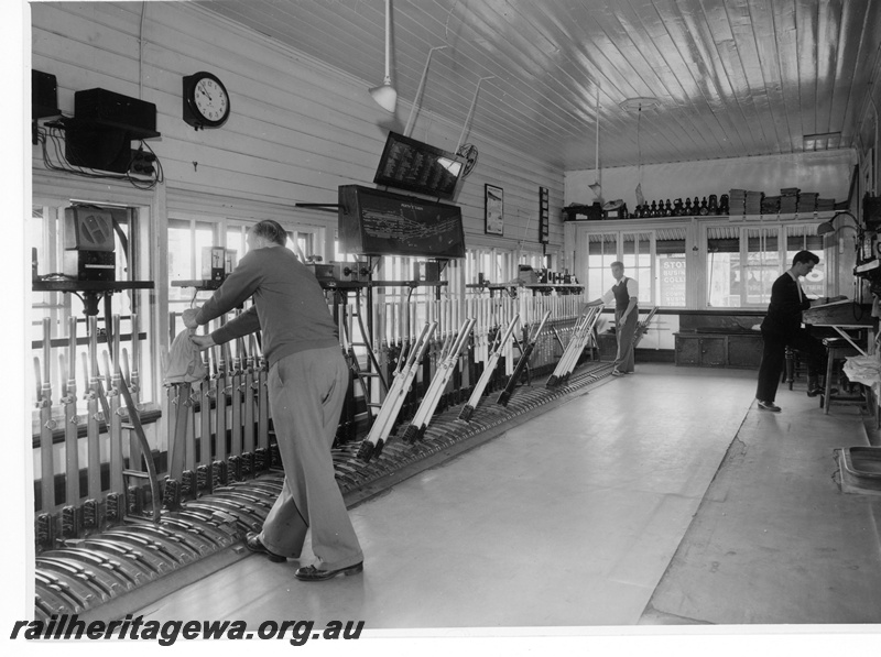 P10771
Signalmen at work setting points and signals in Box C at Perth Station while the 'block boy' makes the required entries in the train register book.
