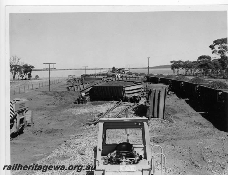 P10943
1 of 2 depicting the aftermath of the derailment of an iron ore train near Southern Cross. 16.3.1973, Clean up work is in progress as a loaded ore train eases past on a detour. See P10919.

