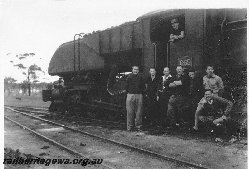 P13471
1 of 3 images taken at Norseman, CE line, of the last steam working on the Coolgardie to Esperance line, ASG class 65 hauled ASG class 55 dead on No.156 goods ex Norseman. View of the cab and rear bunker. Fireman Barry Wintle in the cab, left to right in front of the cab are driver Ron Bradshaw, fireman Gerry Mcintyre, guard Bill Waller, driver Josh Downey, fitter Bill Rayner, fireman Tom Berg and driver Ken Nichols. 
