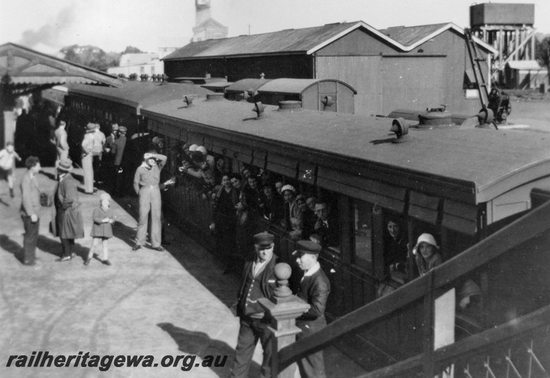 P14465
Side loading country carriage with passengers looking out of the windows, platform and buildings, goods shed, water tower, Narrogin, GSR line, small child on the platform is late ARHS member Brian Morrell, loaded train is possibly a 