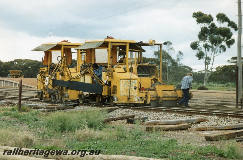 P15269
Mobile track maintenance machine in operation, driver, spectator, used sleepers beside track, Lake Grace, WLG line
