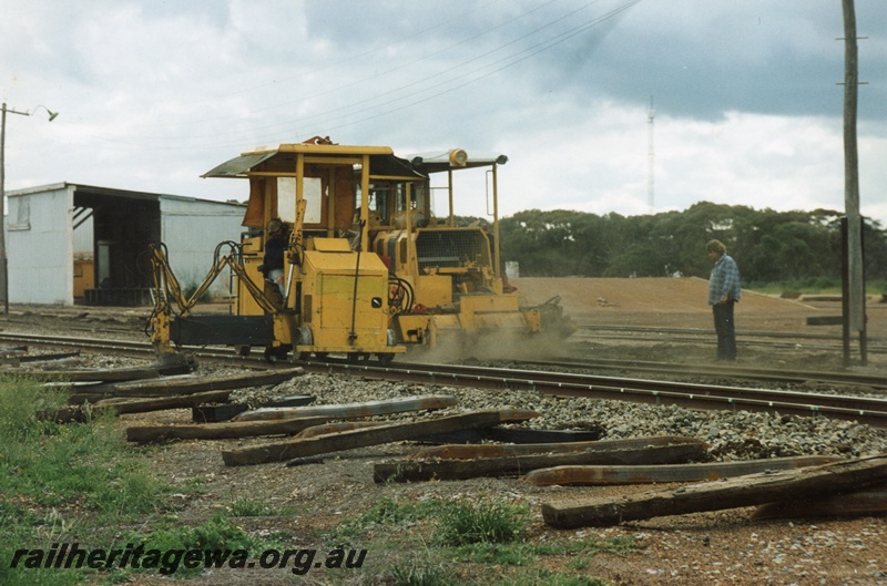 P15270
Mobile track maintenance machine in operation, driver, spectator, used sleepers beside track, shed, Lake Grace, WLG line
