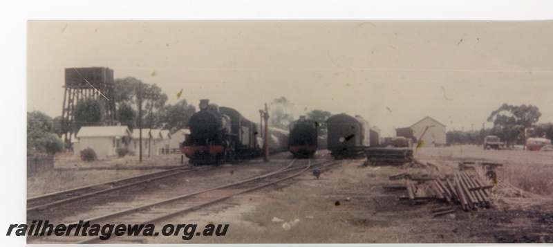 P16372
Station yard, steam locos, rake of carriages, water tower, water column, sleeper pile, spare rails, goods shed, shop, Cunderdin, EGR line, view from east end
