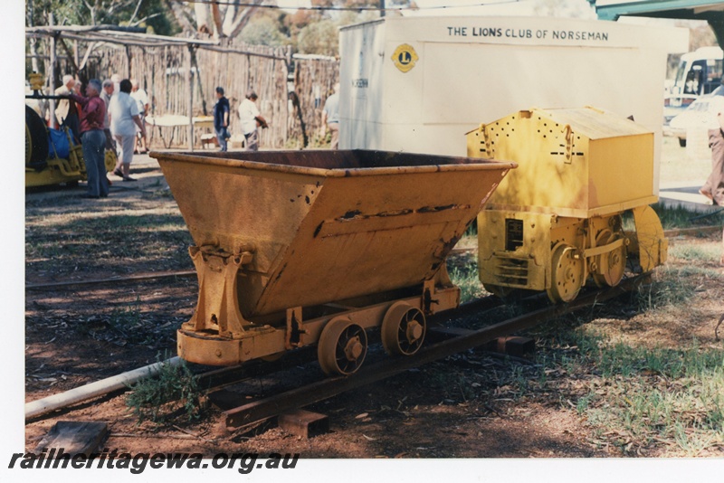 P16521
Small yellow mine tipper wagon, small yellow mine loco, in preservation at Norseman museum, visitors in background, end and side view
