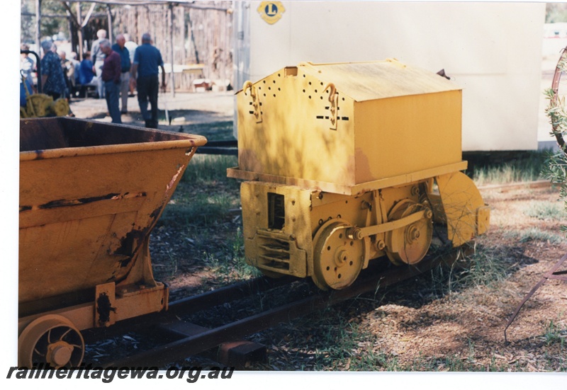 P16522
Small yellow mine loco, in preservation at Norseman museum, visitors in background, end and side view
