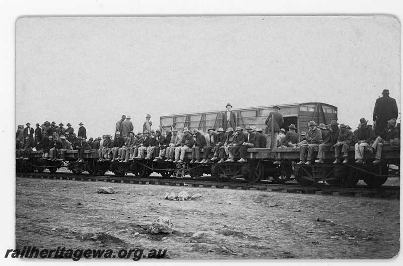 P16803
Commonwealth Railways (CR) - TAR line track workers sitting on flat wagons being transported to work site. c1916
