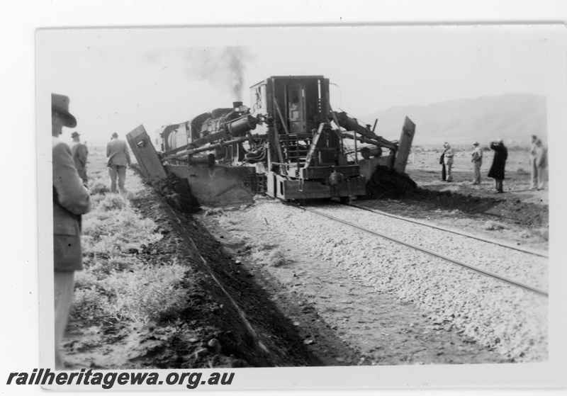 P16859
Commonwealth Railways (CR) - TAR line official inspection of track mounted machine used for digging drains alongside the track being propelled by an L class steam locomotive. 
