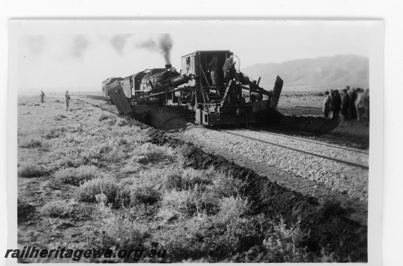 P16860
Commonwealth Railways (CR) - TAR line official inspection of track mounted machine used for digging drains alongside the track being propelled by an L class steam locomotive.
