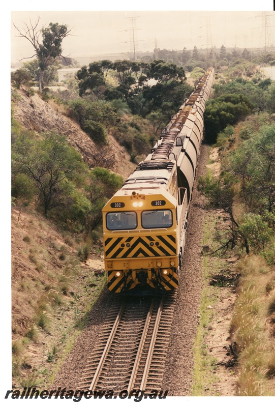 P16941
Q class 302 (relassified Q class 4002) hauls a grain train near Kwinana. Locomotive painted in Westrail yellow livery with black chevrons on front of locomotive. 
