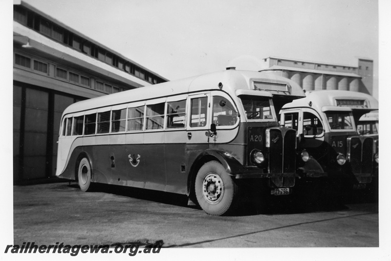 P16989
WAGR Railway Road Service AEC Regal half cab buses numbered A20 and A15, of the type used by the Eastern Goldfields Transport Board, parked outside garage, silo in background, ground level view

