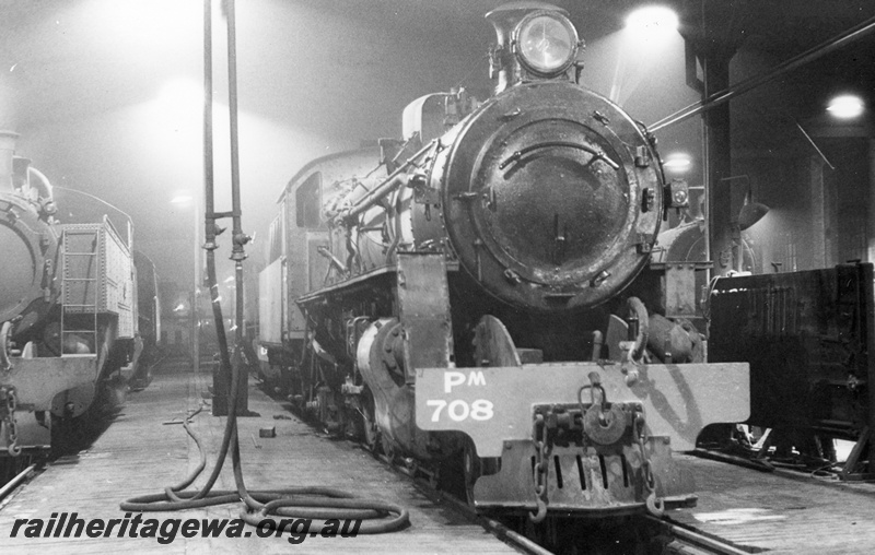 P17129
PM class 708 locomotive, front view in loco shed at East Perth. Unidentified D class tank locomotive to left and possible sand box to right. ER line. 

