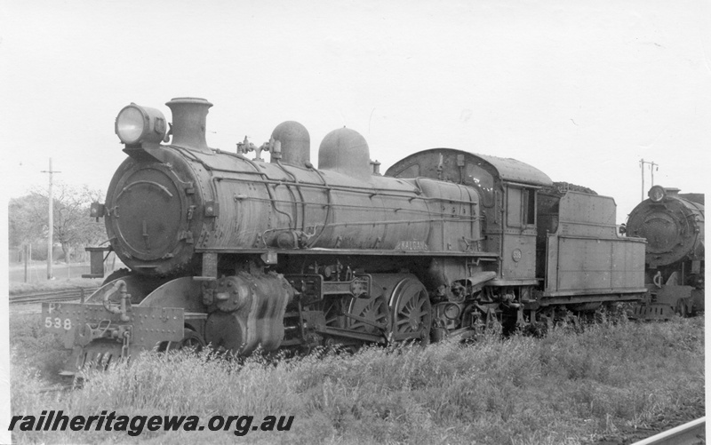 P17151
PR class 538 'Kalgan' locomotive at eastern end of East Perth loco, 3/4 front & side view. Unidentified V class at rear.
