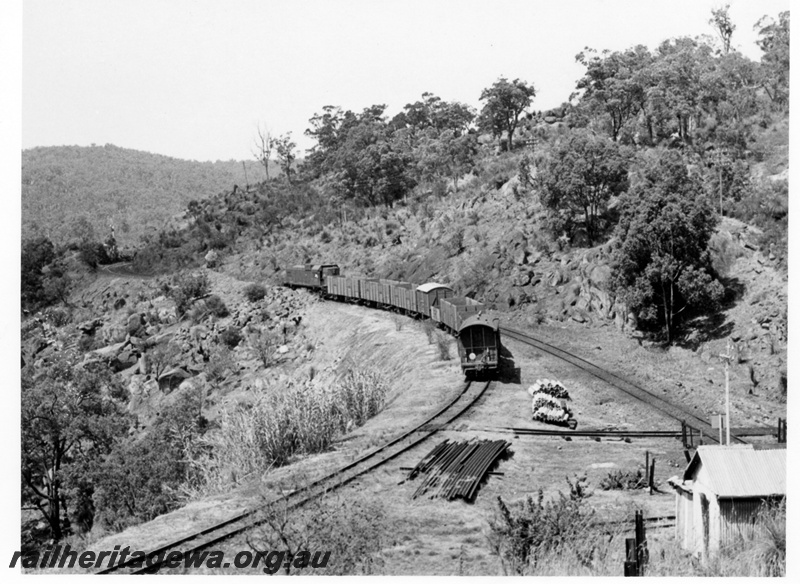 P17596
A short goods train on the eastbound at Tunnel Junction, near Swan View, in the Darling Ranges. ER line. Track Gang shed to right.
