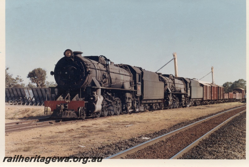 P17834
V class 1221 & 1210 steam locomotives arriving at Popanyinning with 16 goods to cross 17 goods. GSR line. Note grain elevators towering over rear locomotive and freight vehicles. Front and side view of lead locomotive.
