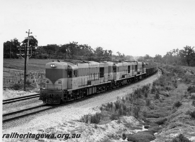 P17840
K class 206 and 2 unidentified standard gauge diesel locomotives hauling 66 loaded iron ore (WO Class) wagons. Location Unknown but may be east of Northam with narrow gauge line to Goomalling parallel to train. View of side of locomotives.
