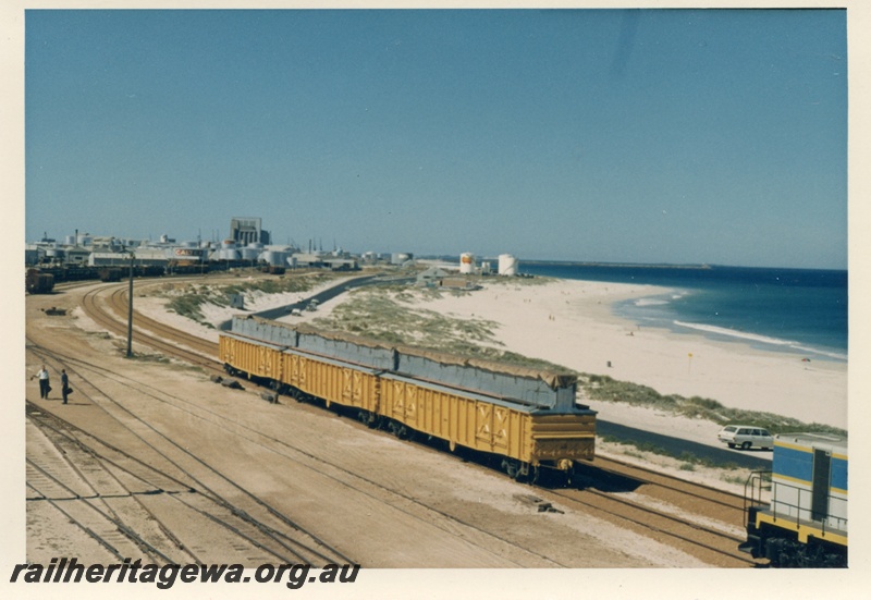 P17988
Rake of three WG class wagons, modified for wheat haulage, Leighton yard, beach, elevated view of the yard looking south, Fremantle port in background, ER line
