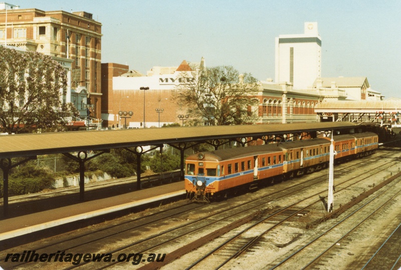 P18069
DMU railcar set comprising ADA, 2 ADG, AYE class cars, platform and canopy, bracket signal, pedestrian overpass, Myer building, Telstra building, Perth city station, c1983 

