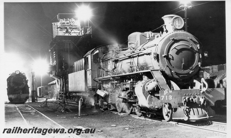 P18224
PM class 713 steam locomotive, side and front view, V class 1202 steam locomotive, front view, coal stage, water column with ladder and platform, fireman's/cleaner's tools on the ground, night-time scene at Narrogin loco, GSR line.
