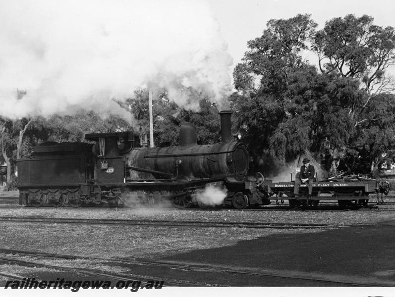 P18234
G class 123 steam locomotive with shunters float NS class 4341 at Busselton. BB line. Note water bag on cab side of locomotive, Curtin in cab window and shunter riding on the float.
