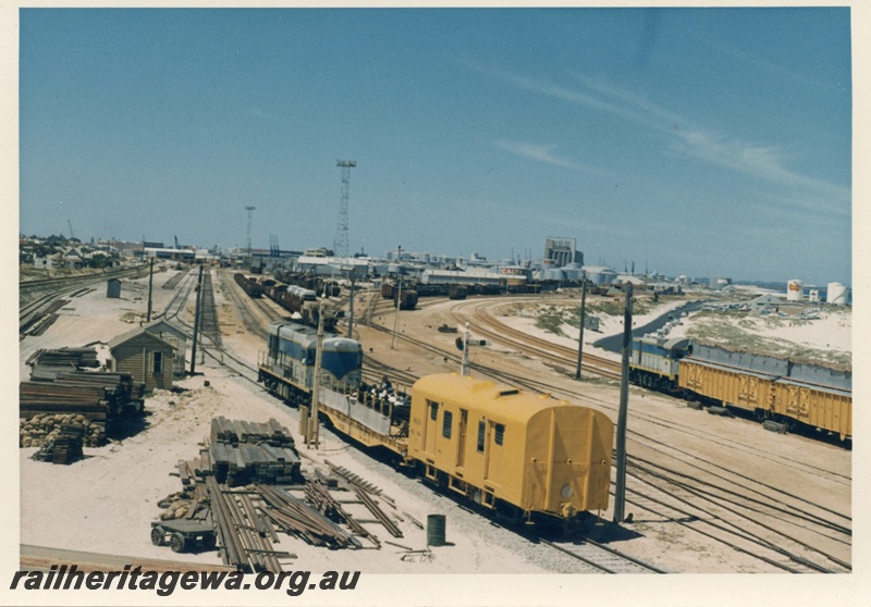 P18298
Diesel hauled standard gauge inspection train leaving Leighton yard, signal, trackside buildings, port of Fremantle in background
