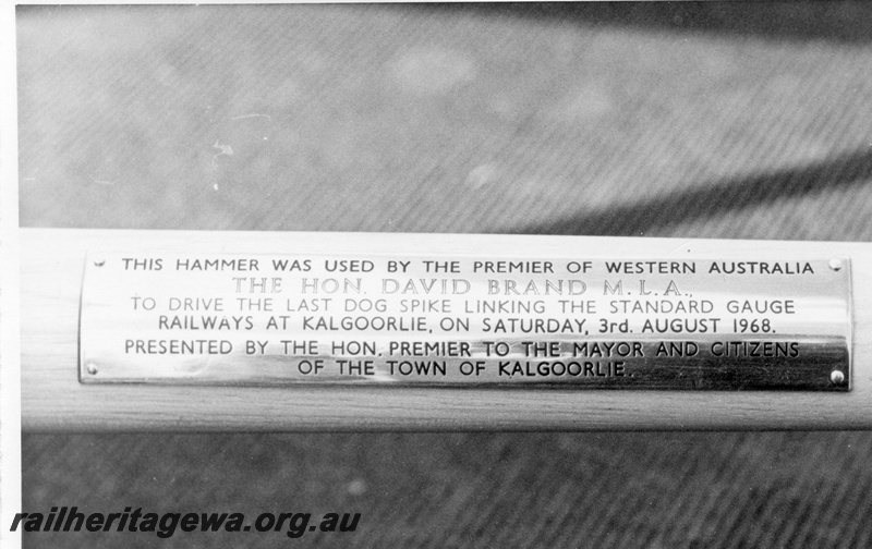 P18473
4 of 12 images relating to the ceremony for the linking of the standard gauge railways at Kalgoorlie, commemorative plaque on the nickel plated hammer used by WA Premier Brand and Mr Ian Sinclair to drive in the final two gold spikes to complete the linking of the standard gauge railways

