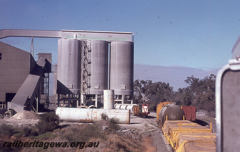 P19812
Y class diesel, on train of van and hoppers being loaded, rake of van, tanker and flat wagons, silos, elevator, conveyor, Soundcem, middle distance view
