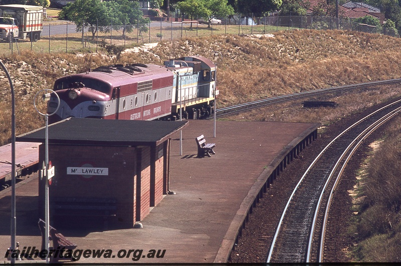 P19831
Unidentified J class diesel in two tone blue and yellow stripe piloting GM class 12 diesel in Commonwealth Railways maroon and silver livery, double heading empty passenger train, passing through station, station shelter, platform, Mount Lawley, ER line, view from elevated position
