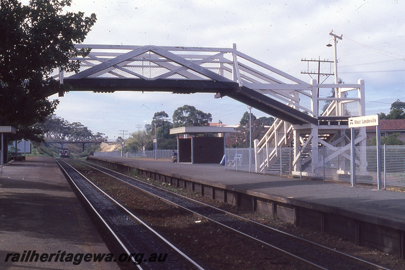 P19855
ADG class railcar set approaching, pedestrian footbridge, platforms, tracks, station shelters, station nameboard, West Leederville, ER line, view  looking towards Perth from platform
