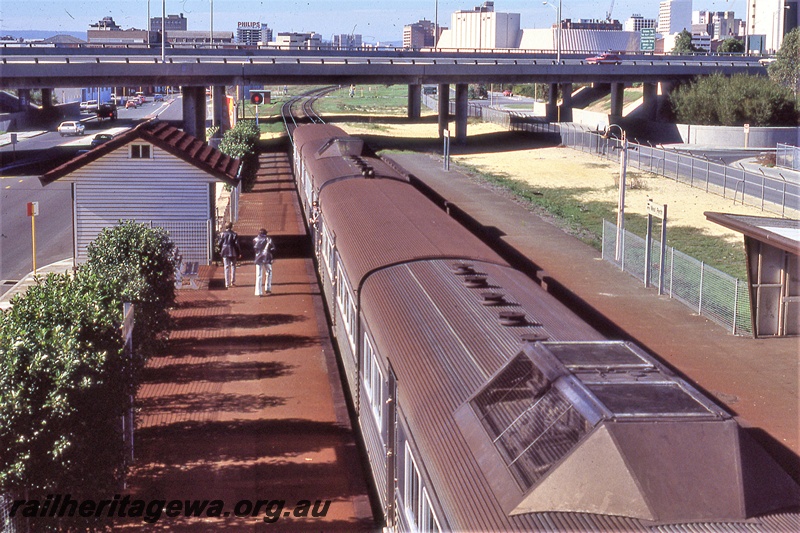 P19859
Stainless steel ADK/ADB class DMU railcar, 4 car set, platforms, station shelters, passengers, road overpass, West Perth, ER line, view from footbridge looking down on railcar roofs 
