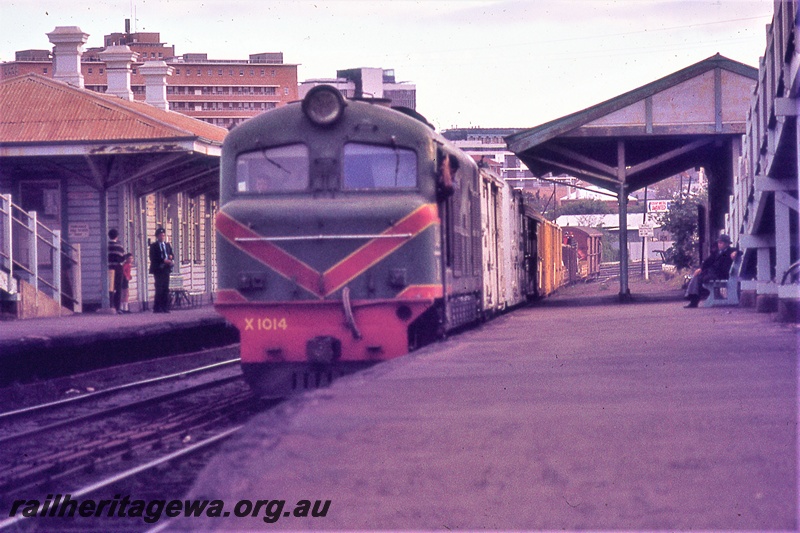 P19860
X class 1014, on goods train, platforms, station buildings, passengers, station attendant ,Claisebrook, ER line, front and side view
