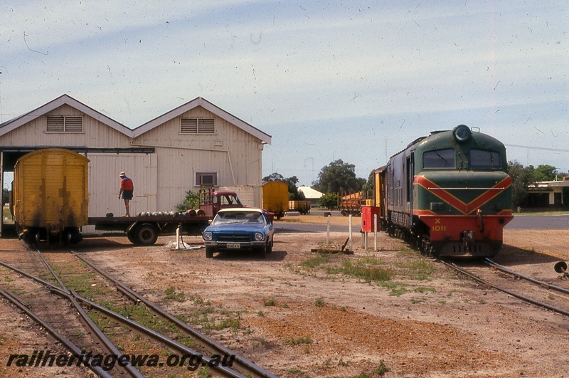 P19969
X class 1011, on goods train, goods shed class 1, truck with man standing on tray, vans, car, road crossing, tracks, Busselton, BB line, side and front view
