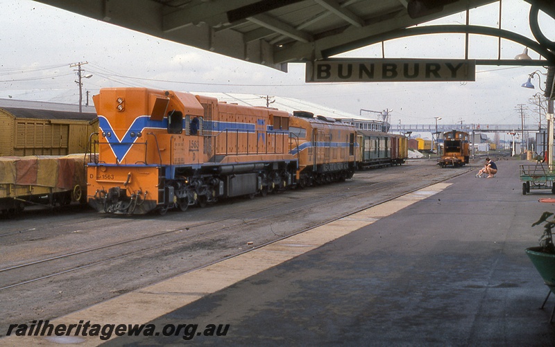 P19985
D class 1563, X class diesel, both in Westrail orange livery with blue and white stripe, diesel shunter in yellow livery, wagon, vans, overhead bridge, signal, tracks, platform, station nameboard, canopy, Bunbury, SWR line
