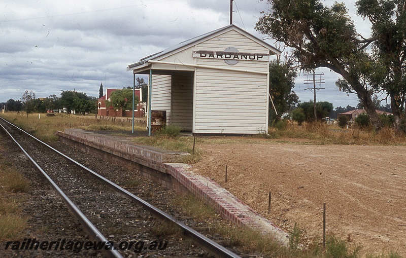 P19992
Station building, station nameboard, platform, track, church, Dardanup, PP line, view from track level
