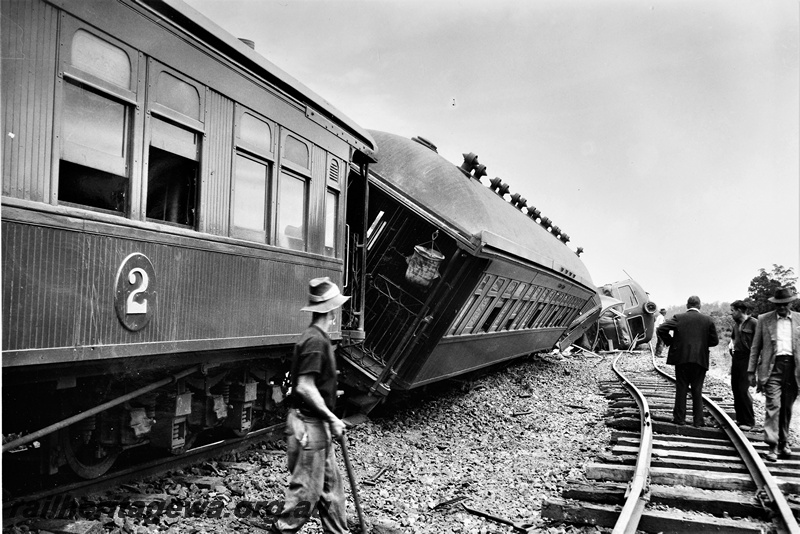 P20361
X class 1005 derailed near Parkerville, ER line,  loco on its side, passenger carriage tilting over, another carriage still on track, twisted track, workers, view from trackside. Se also P21594 & P21595
