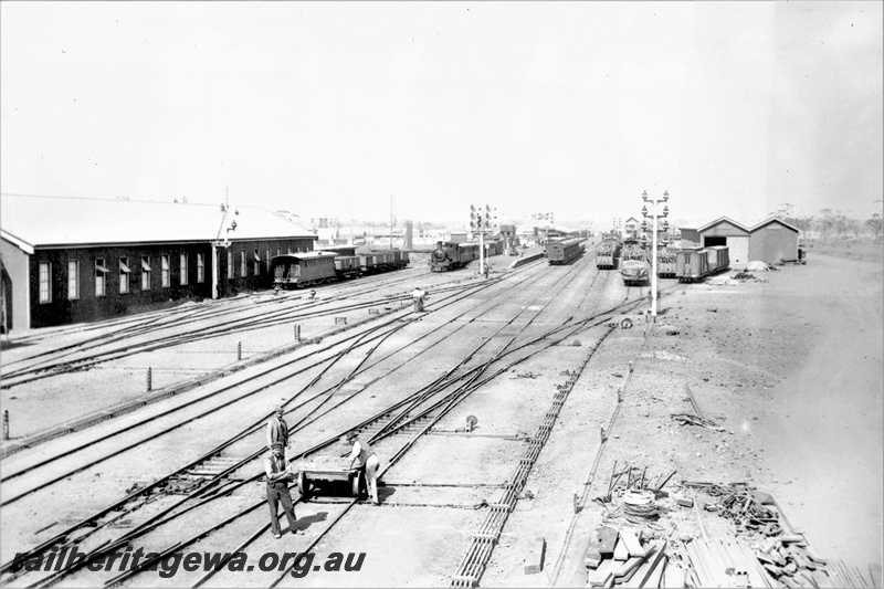 P21929
Yard, rakes of wagons, locos, platform, sidings, pointwork, crossovers, bracket signals, sheds, workers with trolley, view from elevated position
