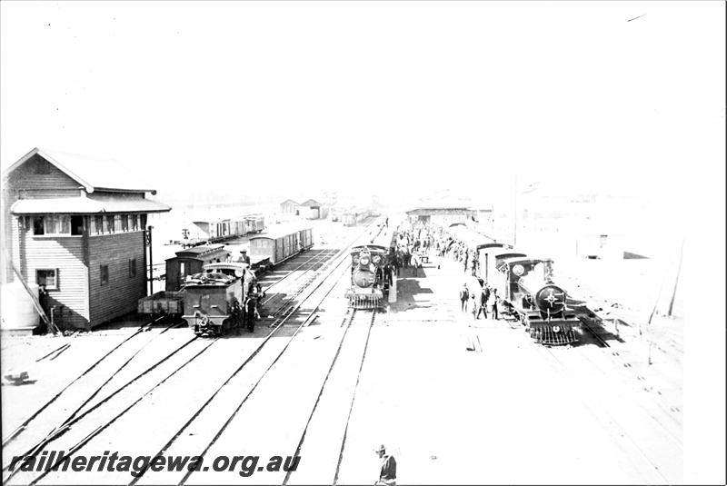 P21930
Steam locos on passenger trains at platform, station building, signal box, another steam loco, rakes of wagons, sheds, tracks, Kalgoorlie, EGR line, view from elevated position

