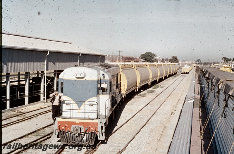 T04697
An unidentified K class standard gauge locomotive with a rake of WW grain hoppers proceeding past the livestock wagons wash point at the eastern end of the former Midland marshalling yard.

