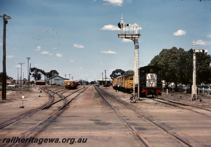 T04879
Station yard, TA class 1814, on maintenance train, workers, signals, points, point levers, sidings, goods shed, station building, platform, road crossing, Katanning, track level view
