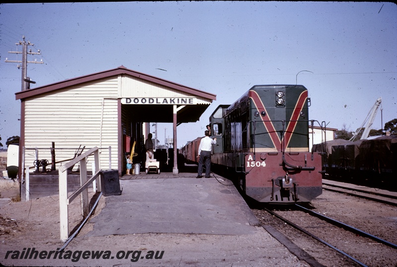 T04923
A class 1504 on No 99 goods train, station building, platform, waiting passengers, goods shed, crane, wagons, Doodlakine, EGR line, station master, G. Proctor changing the staff, note the travelling safe and cream can on the platform.
